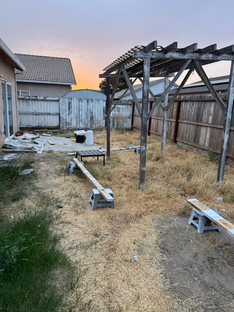 Backyard before: dead patchy grass, bare concrete patio, and weathered fence