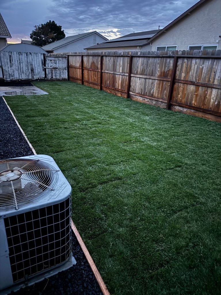 Same backyard after: fresh green sod, new wood fence, and a clean gravel border